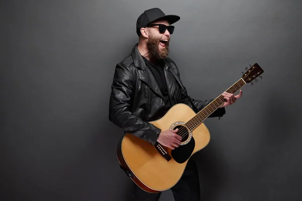 Guitarrista cantando en estudio de música. Guitarrista Hipster con barba y ropa negra tocando la guitarra acústica —  Fotos de Stock