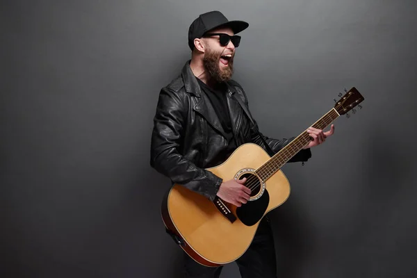 Chitarrista che canta in studio di musica. Chitarrista hipster con barba e vestiti neri che suona la chitarra acustica — Foto Stock