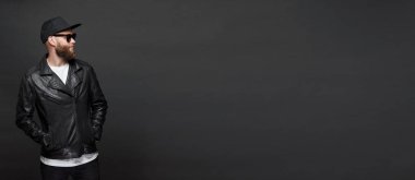 Siyah şapkalı, kot pantolonlu ve güneş gözlüklü deri bisikletçi ceketi veya asimetrik zip ceket giyen adam. Kopya alanı ile gri arka plan üzerinde Yakışıklı hipster adam