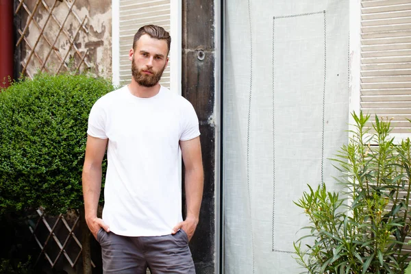 Hipster guapo modelo masculino con barba que lleva una camiseta blanca en blanco con espacio para su logotipo o diseño en estilo urbano casual — Foto de Stock