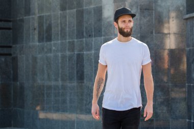 Sakallı, beyaz, boş tişörtlü, beysbol şapkalı, logonuz için yeri olan yakışıklı bir hippi mankeni.