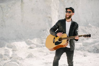 Gitar çalar dışarıda şarkı söylüyor. Sakal ve siyah giysiler ile hipster gitaristi