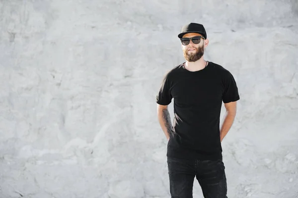 Hipster handsome male model with beard wearing black blank t-shirt with space for your logo or design in casual urban style — Stock Photo, Image