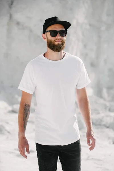 Modelo masculino bonito Hipster com barba vestindo t-shirt branca em branco e um boné de beisebol com espaço para o seu logotipo ou design em estilo urbano casual — Fotografia de Stock