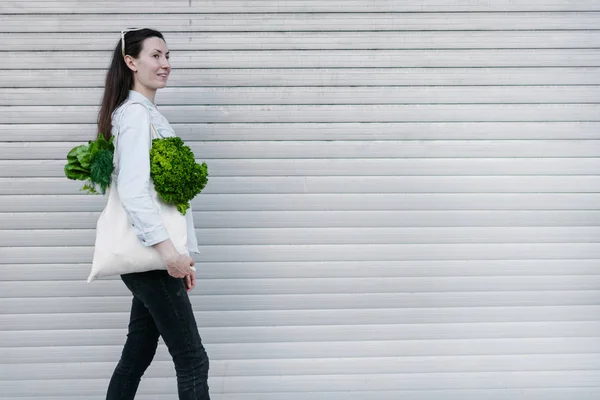 Frau mit einer Öko-Tüte voller Lebensmittel. Gemüse und Obst hängen an einer Tüte. Ökologie oder Umweltschutzkonzept. weiße Öko-Tasche für Attrappen. — Stockfoto