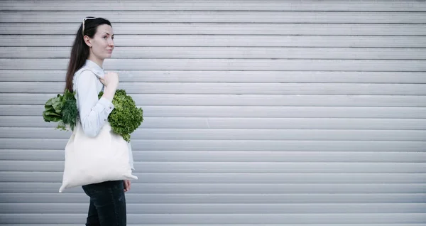 Mulher segurando um saco ecológico cheio de supermercado. Legumes e frutas estão pendurados em um saco. Conceito de ecologia ou de protecção do ambiente. Saco eco branco para simular . — Fotografia de Stock