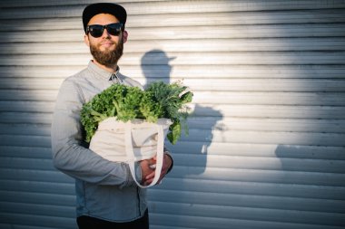 Elinde bakkalla dolu bir eko çanta tutan adam. Sebze ve meyveler torbadan sarkMaktadır. Çevre koruma ekolojisi kavramı