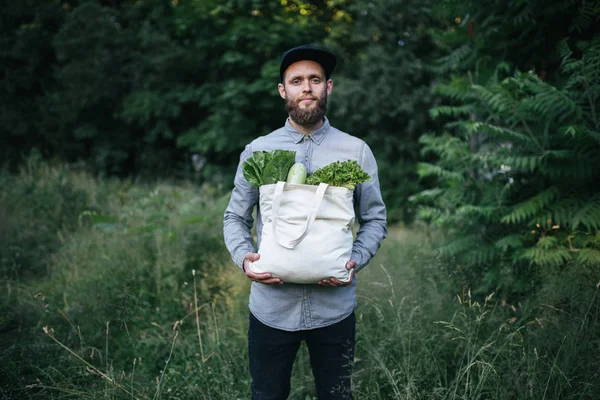 Homem segurando um saco ecológico cheio de supermercado. Legumes e frutas estão pendurados no saco. Conceito ecológico de protecção do ambiente — Fotografia de Stock