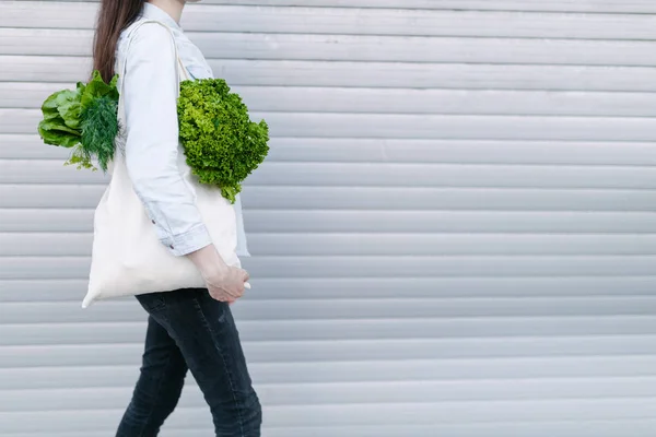 Mujer sosteniendo una bolsa ecológica llena de comestibles. Verduras y frutas cuelgan de una bolsa. Ecología o concepto de protección del medio ambiente. Bolso ecológico blanco para maqueta . — Foto de Stock