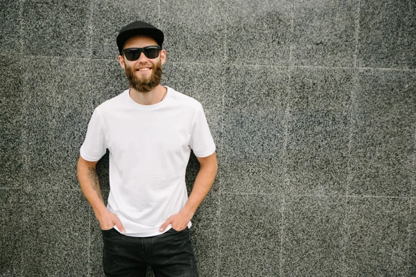 Hipster knappe mannelijke model met baard met witte witte witte t-shirt en een honkbalpet met ruimte voor uw logo of ontwerp in casual stedelijke stijl — Stockfoto