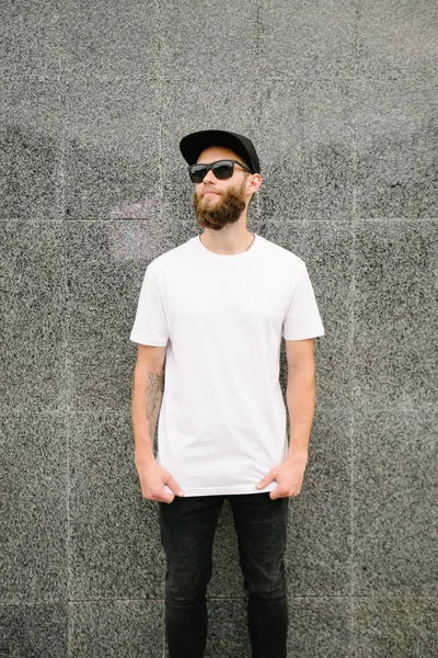 Hipster handsome male model with beard wearing white blank t-shirt and a baseball cap with space for your logo or design in casual urban style — Stock Photo, Image