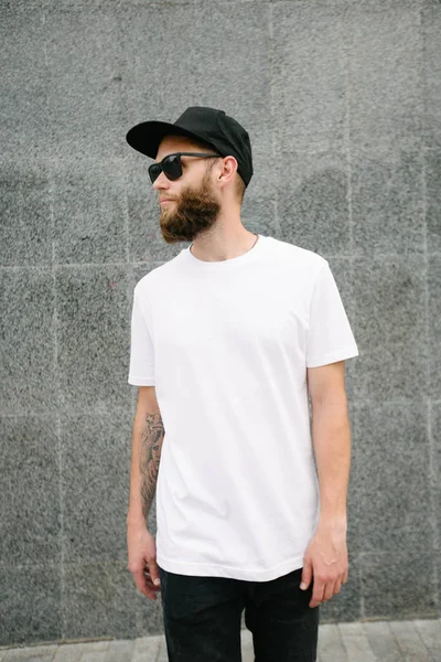 Hipster beau modèle masculin avec barbe portant un t-shirt blanc et une casquette de baseball avec de l'espace pour votre logo ou design dans un style urbain décontracté — Photo