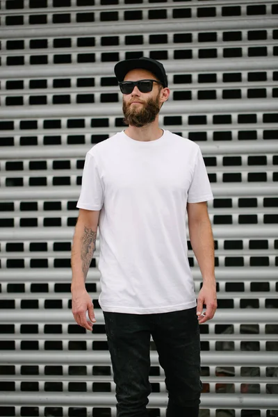 Hipster knappe mannelijke model met baard met witte witte witte t-shirt en een honkbalpet met ruimte voor uw logo of ontwerp in casual stedelijke stijl — Stockfoto