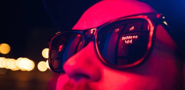 Şehir sokaklarında hipster yakışıklı adam Neon işaretler tarafından aydınlatılmış olmak. O siyah kap, kot pantolon ve güneş gözlüğü ile deri motosikletçi ceket veya asimetrik fermuar ceket giyiyor.