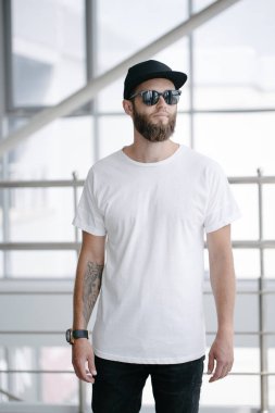 Sakallı, beyaz, boş tişörtlü, beysbol şapkalı, logonuz için yeri olan yakışıklı bir hippi mankeni.