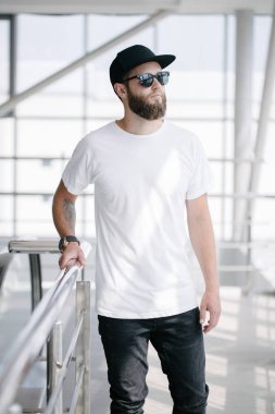 Sakallı, beyaz, boş tişörtlü, beysbol şapkalı, logonuz için yeri olan yakışıklı bir hippi mankeni.