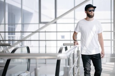 Sakallı, beyaz, boş tişörtlü, beysbol şapkalı, logonuz için yeri olan yakışıklı bir hippi mankeni.