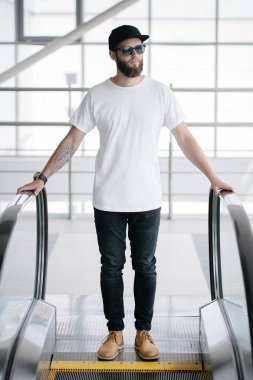 Sakallı, beyaz, boş tişörtlü, beysbol şapkalı, logonuz için yeri olan yakışıklı bir hippi mankeni.