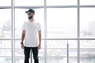 Sakallı, beyaz, boş tişörtlü, beysbol şapkalı, logonuz için yeri olan yakışıklı bir hippi mankeni.