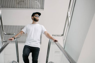 Sakallı, beyaz, boş tişörtlü, beysbol şapkalı, logonuz için yeri olan yakışıklı bir hippi mankeni.