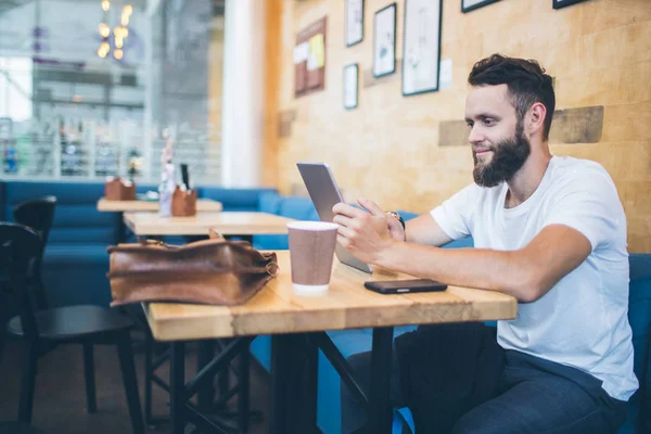 Man använder en Tablet PC på en restaurang eller kaffe plats. Han bär vit t-shirt och sitter vid ett bord — Stockfoto