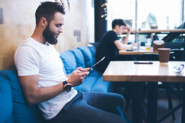 Homem usando um tablet pc em um restaurante ou café. Ele está vestindo t-shirt branca e sentado a uma mesa — Fotografia de Stock