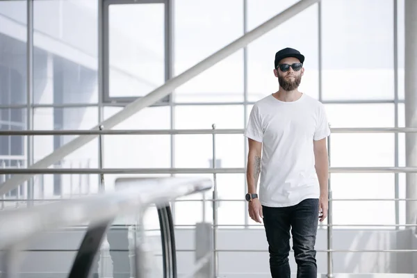 Hipster beau modèle masculin avec barbe portant un t-shirt blanc et une casquette de baseball avec de l'espace pour votre logo ou design dans un style urbain décontracté — Photo