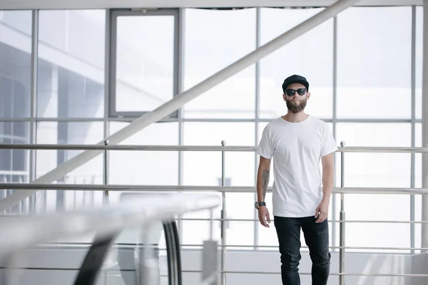 Hipster handsome male model with beard wearing white blank t-shirt and a baseball cap with space for your logo or design in casual urban style — Stock Photo, Image