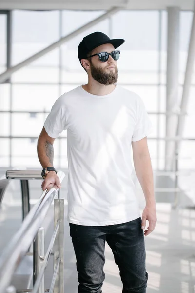 Hipster beau modèle masculin avec barbe portant un t-shirt blanc et une casquette de baseball avec de l'espace pour votre logo ou design dans un style urbain décontracté — Photo