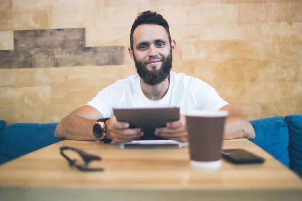 Ember használ egy tabletta PC-ban egy vendéglő vagy kávé hely. Fehér pólót visel, és asztalnál ül — Stock Fotó