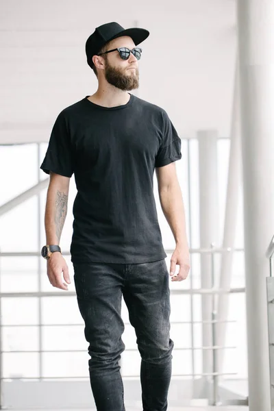 Hipster handsome male model with beard wearing black blank t-shirt with space for your logo or design in casual urban style — Stock Photo, Image