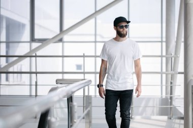 Sakallı, beyaz, boş tişörtlü, beysbol şapkalı, logonuz için yeri olan yakışıklı bir hippi mankeni.