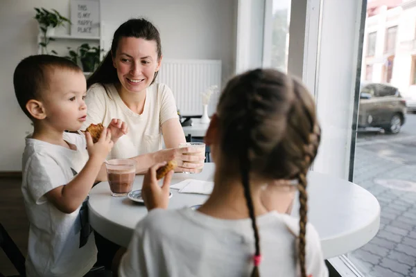 Moeder met kinderen die warme chocolademelk en Latte drinken in een lokale koffieshop. Ze glimlachen en hebben plezier. — Stockfoto