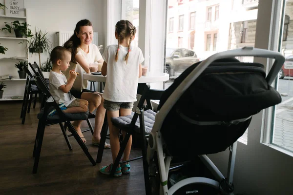 Madre con bambini che beve cioccolata calda e latte macchiato in una caffetteria locale. Sorridono e si divertono . — Foto Stock