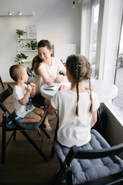 Moeder met kinderen die warme chocolademelk en Latte drinken in een lokale koffieshop. Ze glimlachen en hebben plezier. — Stockfoto