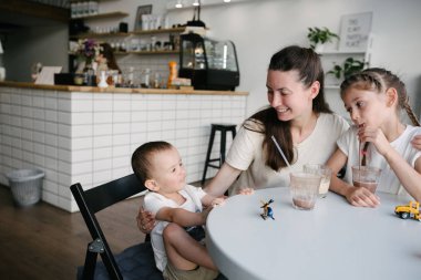Yerel bir kafede sıcak çikolata ve latte içen çocuklu bir anne. Gülümsüyorlar ve eğleniyorlar..