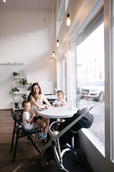 Madre con niños bebiendo chocolate caliente y café con leche en una cafetería local. Ellos sonríen y se divierten . — Foto de Stock