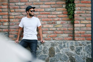 Sakallı, beyaz, boş tişörtlü, beysbol şapkalı, logonuz için yeri olan yakışıklı bir hippi mankeni.