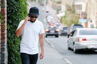 Sakallı, beyaz, boş tişörtlü, beysbol şapkalı, logonuz için yeri olan yakışıklı bir hippi mankeni.