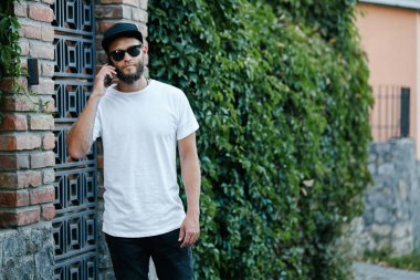 Sakallı, beyaz, boş tişörtlü, beysbol şapkalı, logonuz için yeri olan yakışıklı bir hippi mankeni.