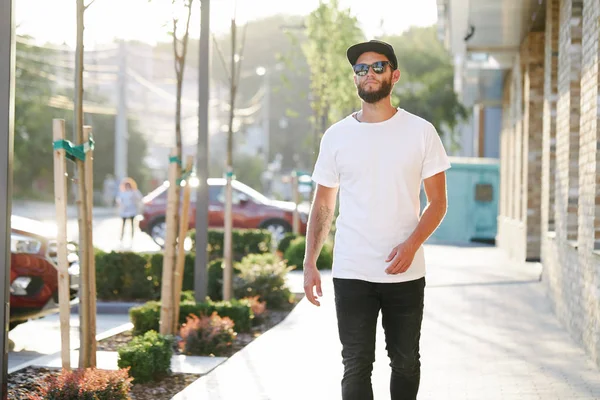 Modelo masculino bonito Hipster com barba vestindo t-shirt branca em branco e um boné de beisebol com espaço para o seu logotipo ou design em estilo urbano casual — Fotografia de Stock