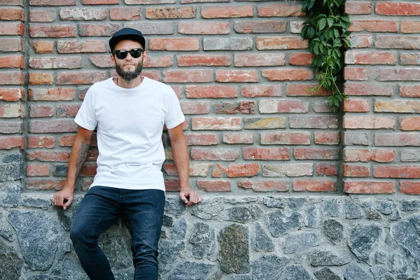 Hipster handsome male model with beard wearing white blank t-shirt and a baseball cap with space for your logo or design in casual urban style — Stock Photo, Image