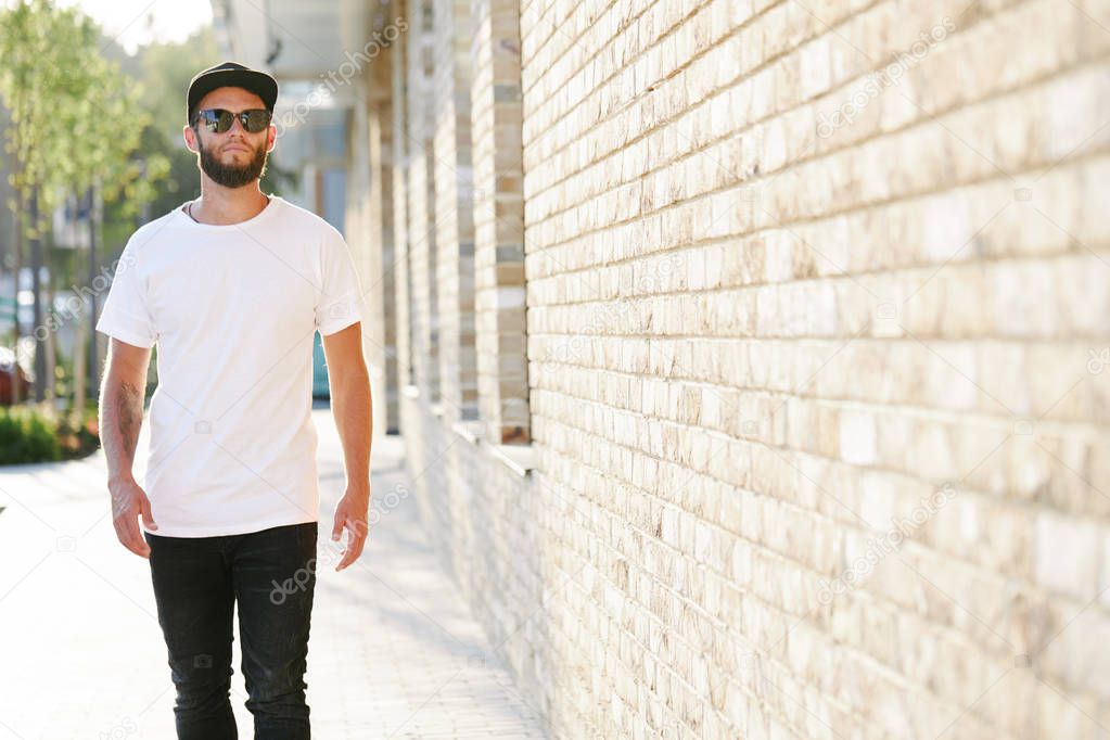 Hipster handsome male model with beard wearing white blank t-shirt and a baseball cap with space for your logo or design in casual urban style