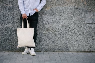 Kentsel şehir arka plan karşı beyaz tekstil eko çanta tutan genç adam. . Ekoloji veya çevre koruma kavramı. Sahte için beyaz eko çanta.