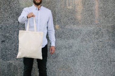 Kentsel şehir arka plan karşı beyaz tekstil eko çanta tutan genç adam. . Ekoloji veya çevre koruma kavramı. Sahte için beyaz eko çanta.