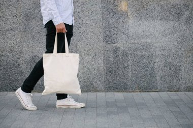 Kentsel şehir arka plan karşı beyaz tekstil eko çanta tutan genç adam. . Ekoloji veya çevre koruma kavramı. Sahte için beyaz eko çanta.