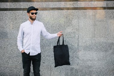 Kentsel şehir arka plan karşı siyah tekstil eko çanta tutan genç adam. . Ekoloji veya çevre koruma kavramı. Tasarım veya logo sahte için siyah eko çanta