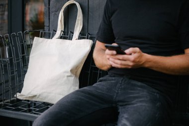 Kentsel şehir arka plan karşı beyaz tekstil eko çanta tutan genç adam. . Ekoloji veya çevre koruma kavramı. Sahte için beyaz eko çanta.