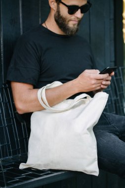 Kentsel şehir arka plan karşı beyaz tekstil eko çanta tutan genç adam. . Ekoloji veya çevre koruma kavramı. Sahte için beyaz eko çanta.