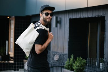 Kentsel şehir arka plan karşı beyaz tekstil eko çanta tutan genç adam. . Ekoloji veya çevre koruma kavramı. Sahte için beyaz eko çanta.